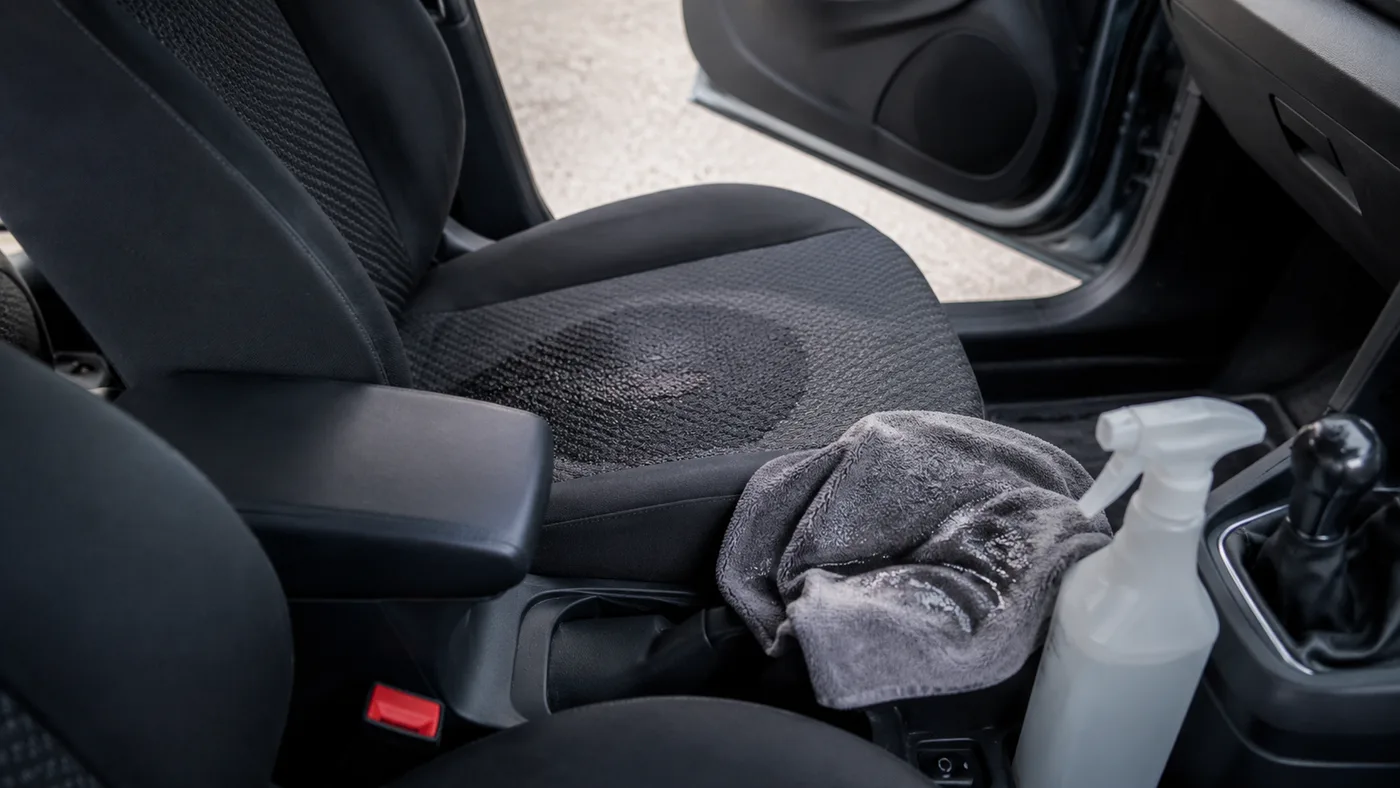 Stoff-Autositz nach der Reinigung mit Mikrofasertuch und Sprühflasche auf der Mittelkonsole, Tür offen für Belüftung
