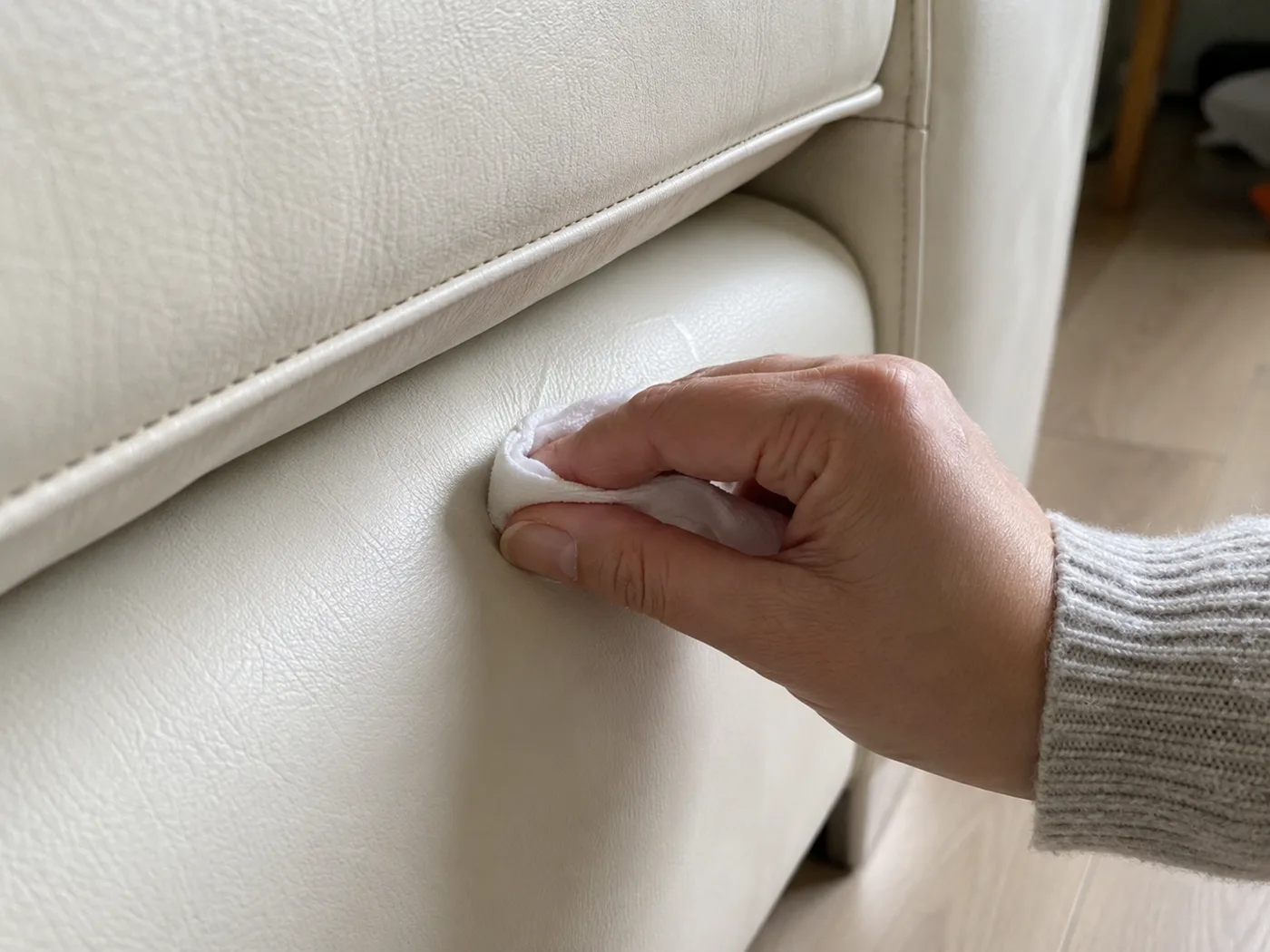 Hand testet mit einem zusammengefalteten weißen Tuch eine unauffällige Stelle an einem weißen Kunstleder-Sofa